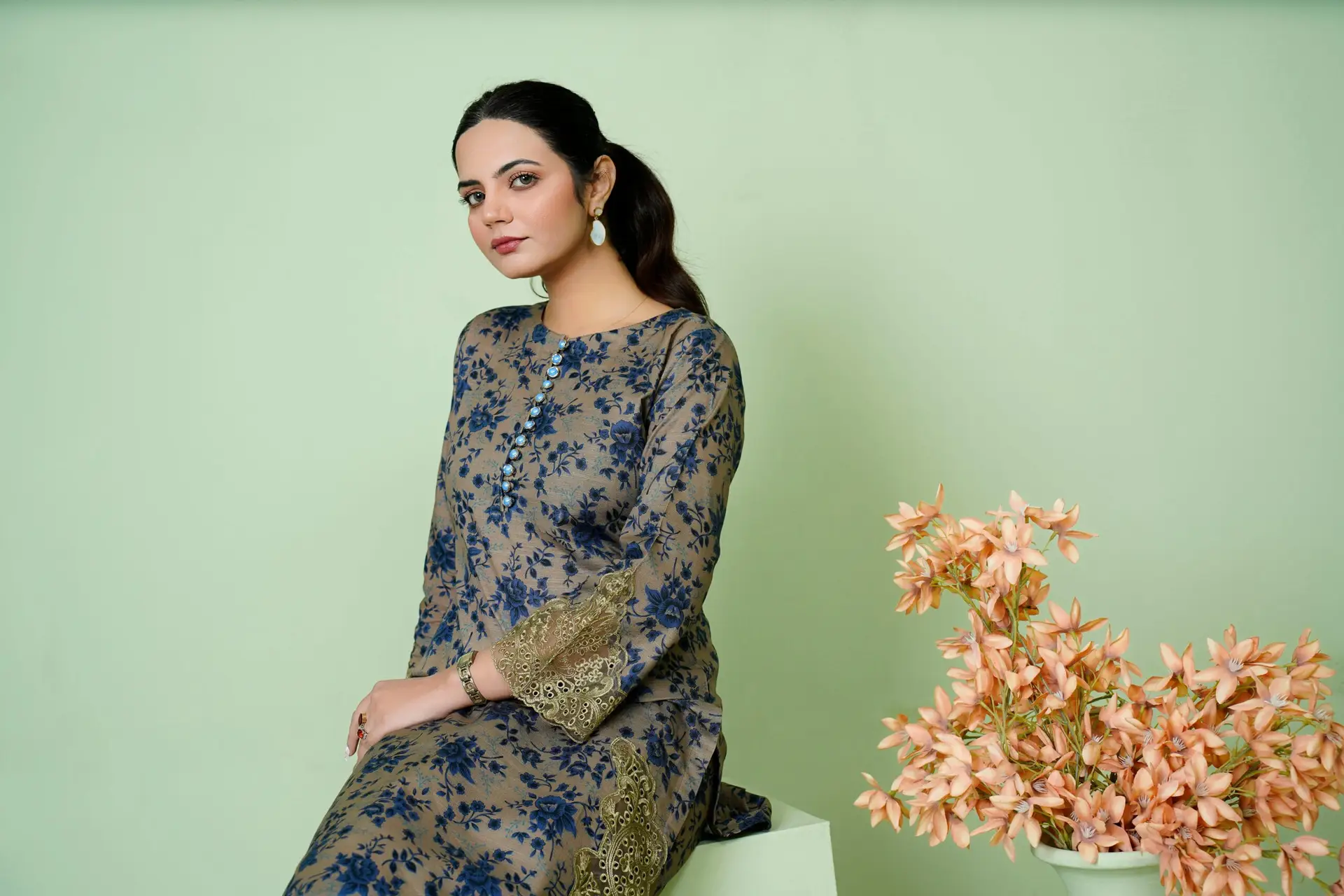 Young woman in floral embroidered dress posing with flowers indoors.