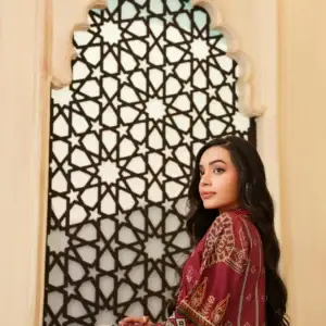 Young woman in a traditional Pakistani dress standing in front of ornate lattice window.